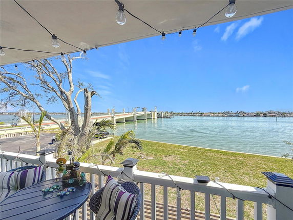 View of a body of water with a bridge and trees in the background, seen from a balcony with seating.
