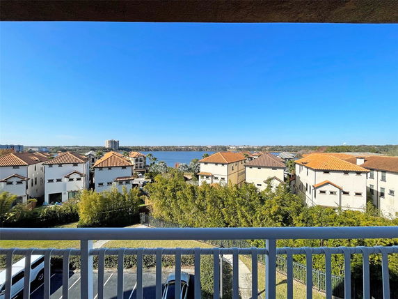 Wide-angle view from a balcony overlooking a residential area with lake and buildings in the background.