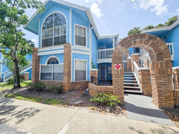 Front view of a blue two-story house with arched windows and a brick entrance archway.