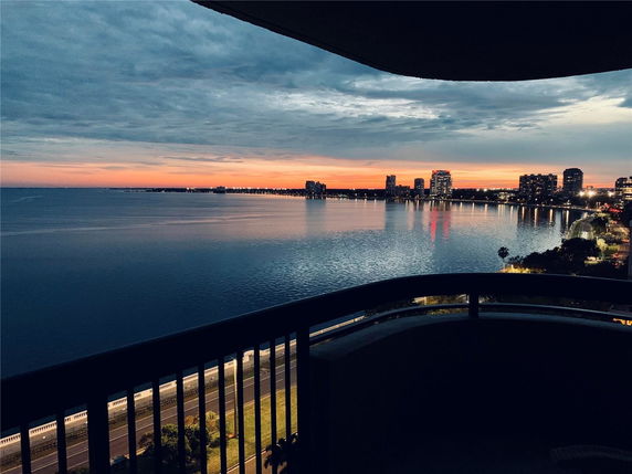 Panoramic view from a balcony overlooking a body of water with city skyline in the distance at sunset.