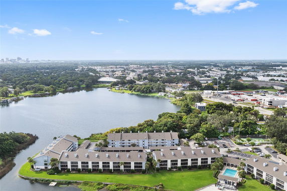 Aerial view of a complex of residential buildings by a large body of water, with a cityscape in the background.