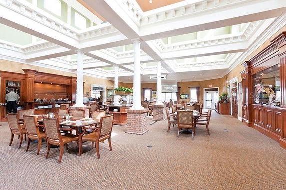 Spacious indoor common area with dining tables and chairs, featuring large white pillars and a high ceiling with decorative moldings.