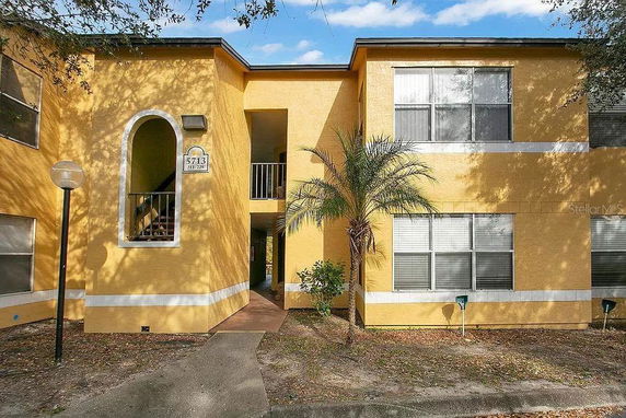 Front view of a two-story yellow apartment building with large windows and a staircase entry.
