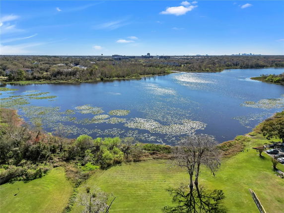 Panoramic view of a lake surrounded by greenery with distant cityscape.