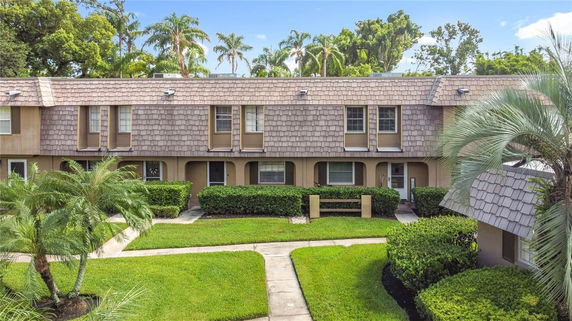 Front view of a two-story townhouse with a shingled roof and landscaped garden.