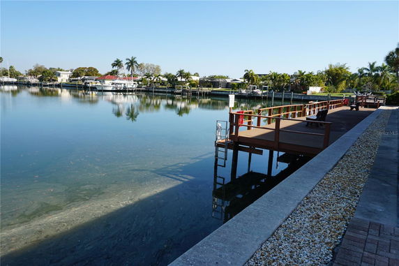 View of a calm waterway with boats docked alongside, surrounded by palm trees and residential buildings.