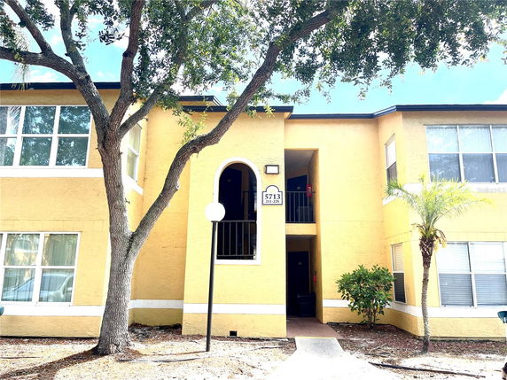 Front view of a two-story apartment building with yellow exterior and arched entryway.