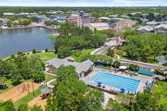 Panoramic view of a recreational area with a swimming pool, playground, and surrounding community buildings near a lake.