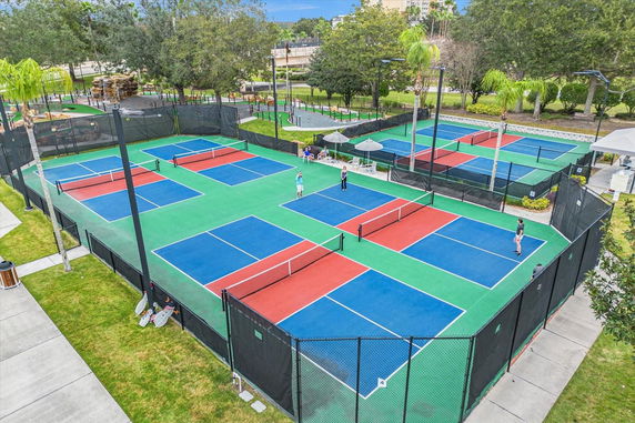 Aerial view of multiple colorful outdoor tennis courts with players and surrounding greenery.