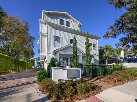 Front view of a multi-story house with a small entrance gate and landscaped shrubs.