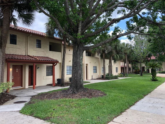Front view of a two-story residential building with red-tiled roofs and trees in the foreground.