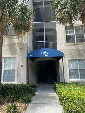 Entrance to a multi-story building with a blue awning and screened balcony.