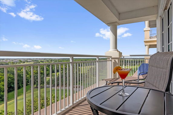 Outdoor balcony with chairs and a table featuring a drink, overlooking a green landscape.