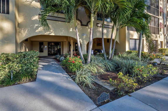 Front view of a building entrance with palm trees and landscaped garden.