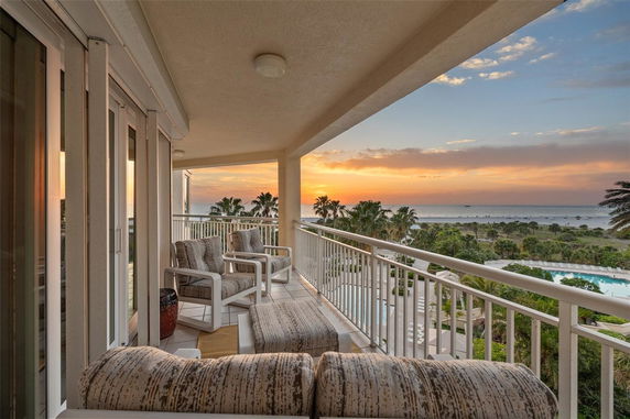 Balcony with comfortable seating overlooking a beach with a sunset view.