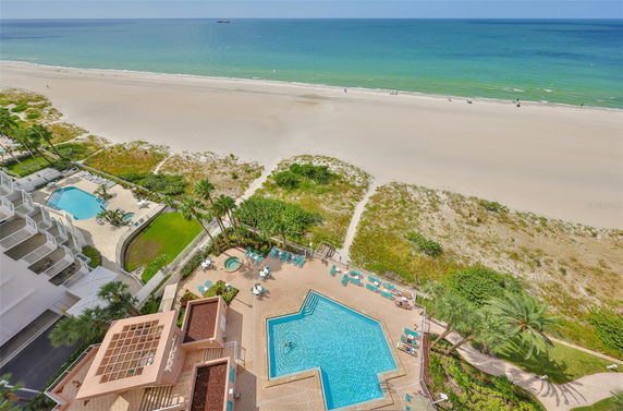 Aerial view of a beachfront with a swimming pool and tiled deck area, overlooking the ocean and sandy beach.