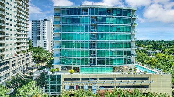 Front view of a modern multi-story building with green glass facade and balconies.