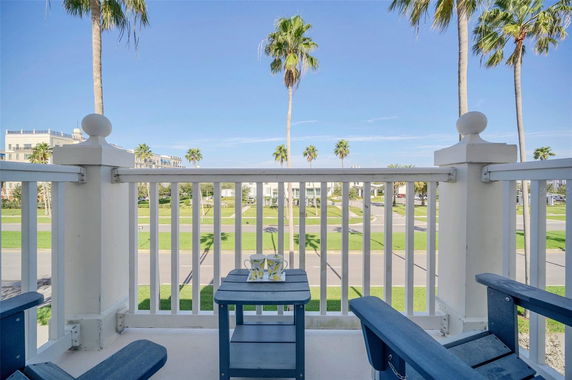 View from a balcony with chairs and table overlooking a street lined with palm trees.