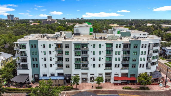 Front view of a multi-story apartment building with balconies and shops at street level.