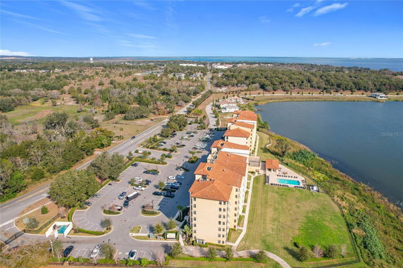 Aerial view of a multi-story building complex near a lake with parking and surrounding landscape.