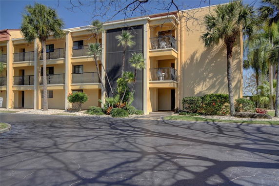 Front view of a three-story apartment building with balconies and palm trees.