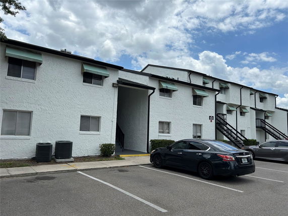 Front view of a two-story residential building with external staircases and parking spaces.