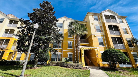 Front view of a multi-story yellow apartment building with balconies.