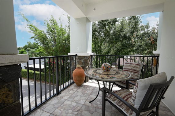 View from a balcony with a mosaic table, two chairs, and decorative pottery, overlooking greenery and trees.