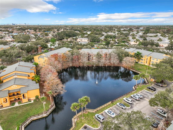 Aerial view of residential buildings surrounding a small lake with a fountain in an urban area.