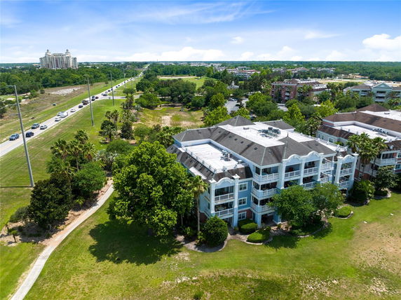 Building with multiple stories and balconies, surrounded by green areas and nearby road.