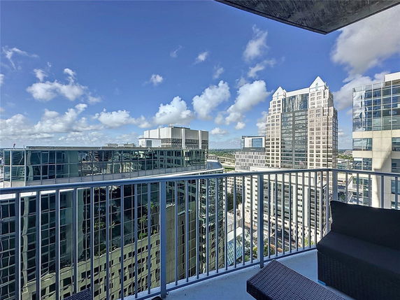 Panoramic view from a high-rise balcony overlooking multiple modern skyscrapers and a clear blue sky.