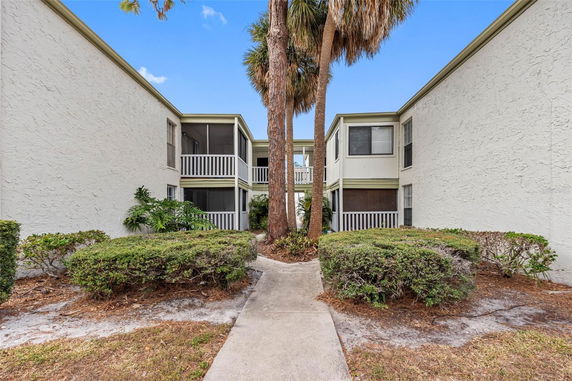 View of a two-story residential building with screened balconies and a walkway.