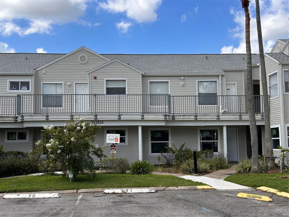 Front view of a two-story building with a balcony and parking spaces.