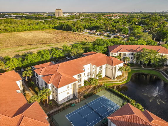 Aerial view of apartment buildings with tennis courts and a pond.