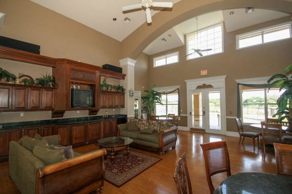 Interior view of a clubhouse with sofas, chairs, a TV, and large windows.