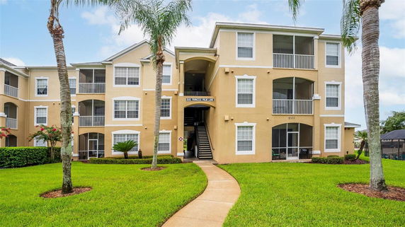 Front view of a three-story apartment building with balconies and a staircase entrance.