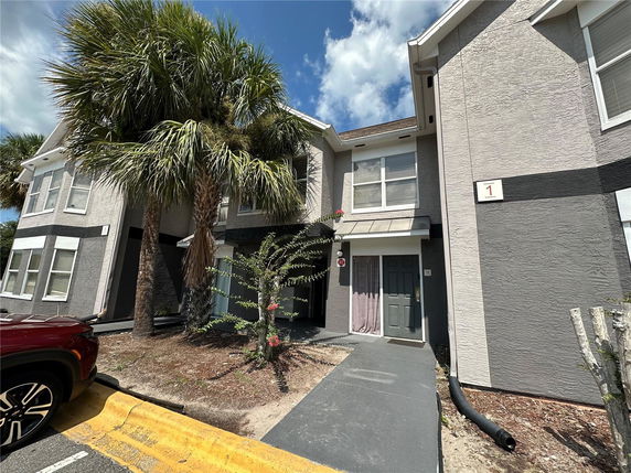 Front view of a multi-story residential building with a gray exterior and palm trees.