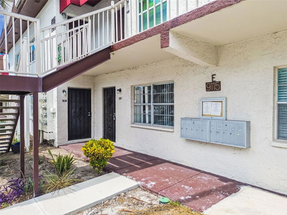 Front view of an apartment building with external stairs and a row of mailboxes.