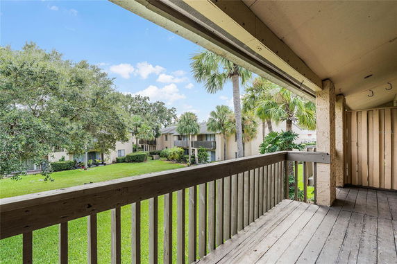 View from a balcony overlooking a grassy area and buildings with palm trees.