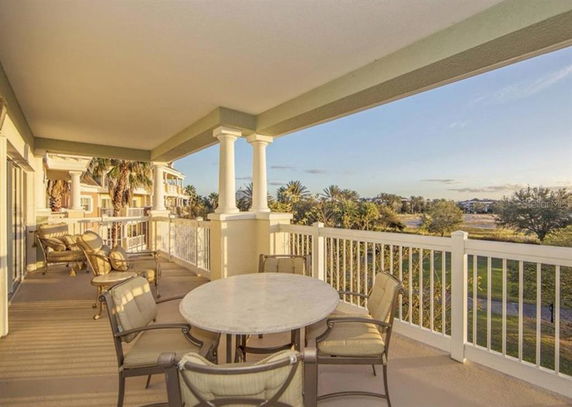 Covered outdoor balcony area with seating and a view of trees and distant landscape.