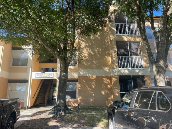 Front view of a multi-story apartment building with balconies and trees in the foreground.