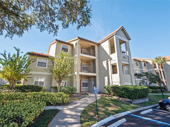 Front view of a multi-story apartment building with a beige exterior and red-tiled roof.