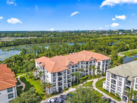 Aerial view of an apartment complex with red and green roofs, surrounded by greenery and water bodies.