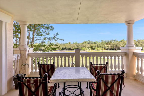 Outdoor seating area with a table and chairs on a balcony overlooking greenery.