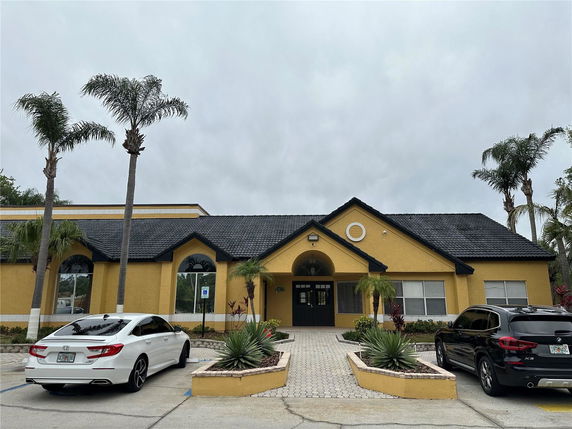 Front view of a building with a prominent entrance and a tiled roof, flanked by palm trees.
