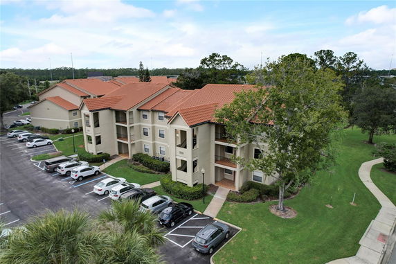 Front view of a multi-story building with beige walls and red tile roofs, surrounded by a parking lot.