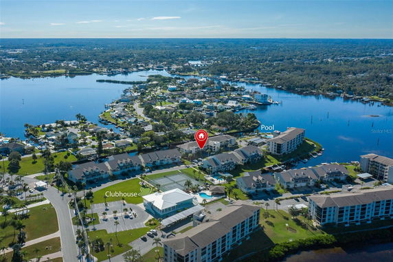 Aerial view of a residential area near a water body with a pool and clubhouse visible.