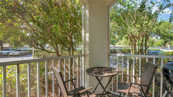Outdoor view from a balcony with a table and chairs overlooking parked cars and trees.