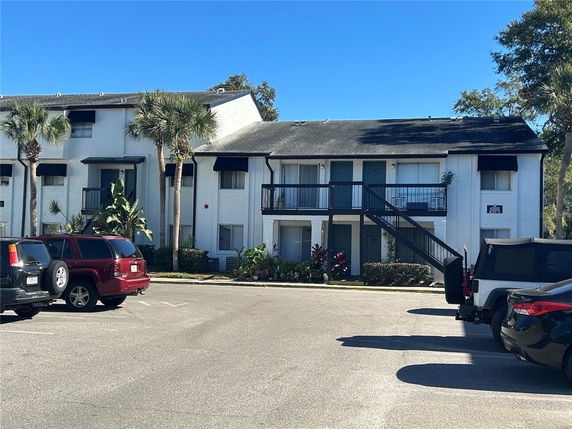 Front view of a two-story apartment building with exterior stairs and a parking area in front.