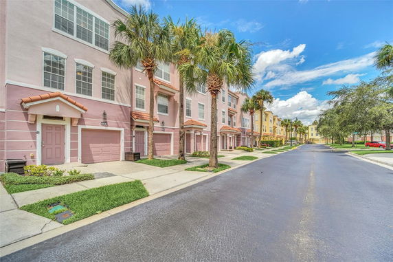 Front view of a row of three-story townhouses with garages and palm trees lining the street.
